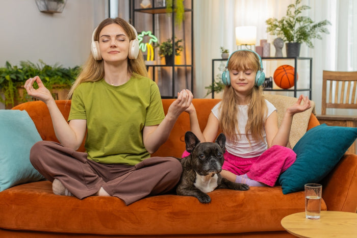 Woman and child meditating on a couch with a dog, wearing headphones.